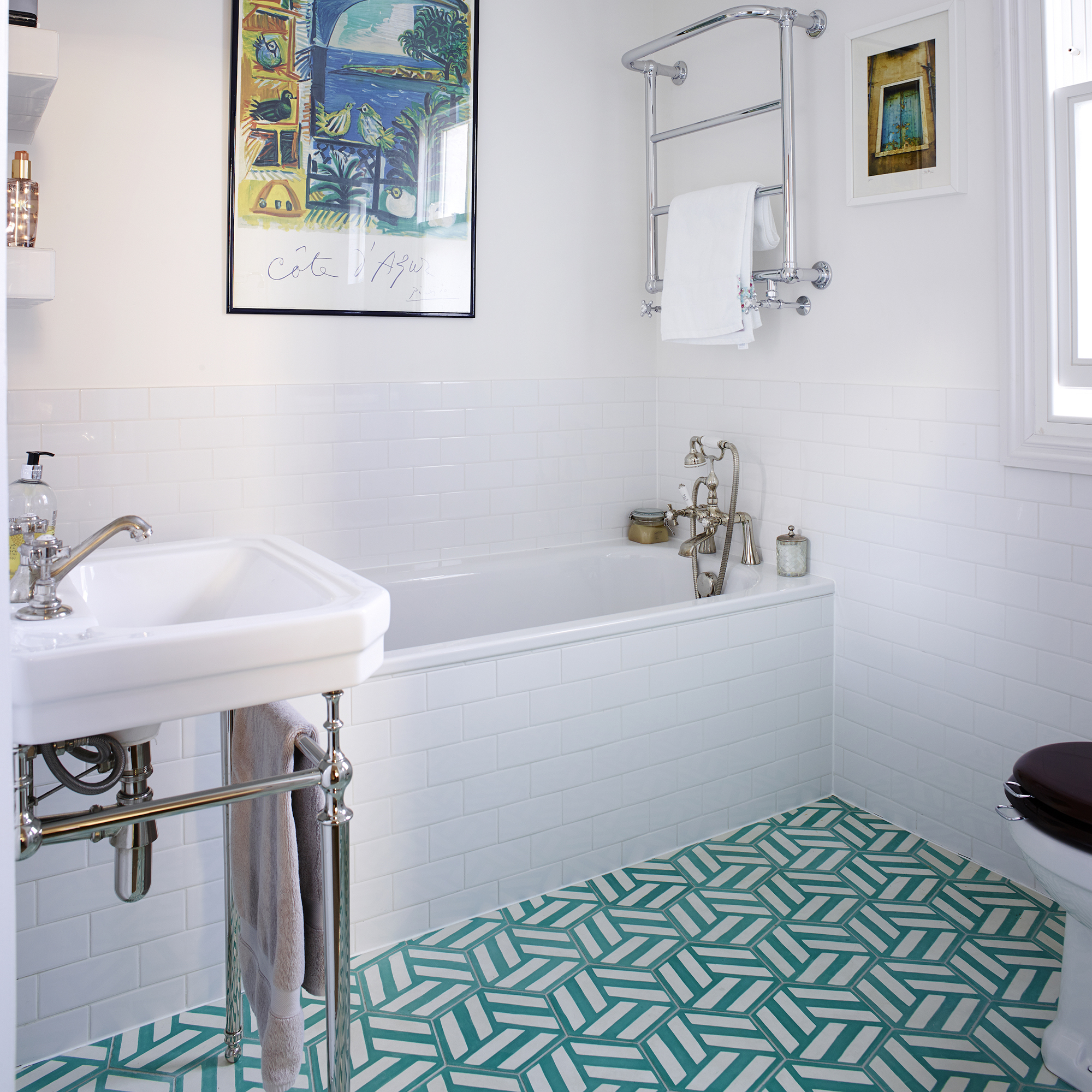 Baño blanco con azulejos geométricos verdes en el suelo y azulejos blancos en la pared y en el borde de la bañera