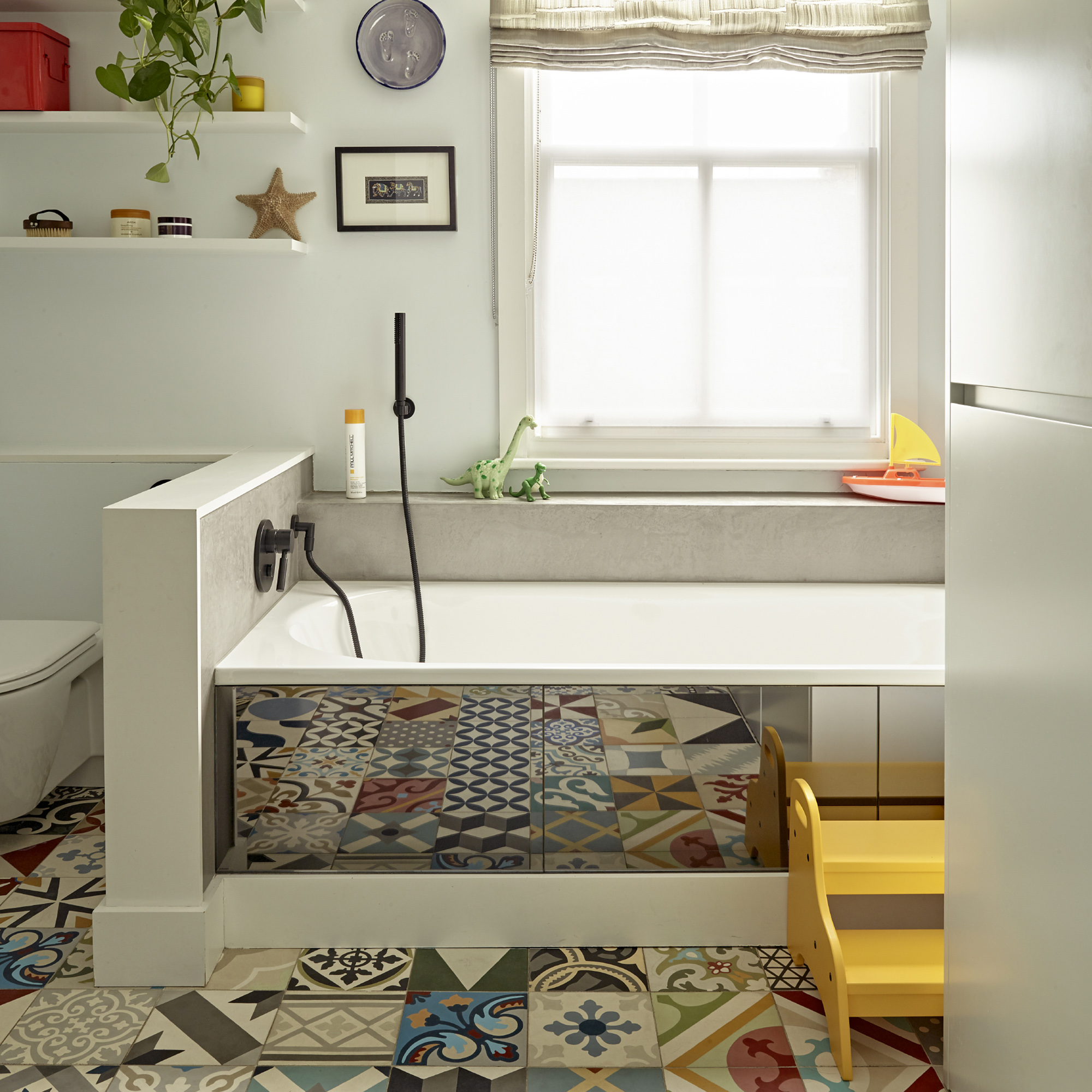 Cuarto de baño con azulejos de colores reflejados en un panel de baño con espejo