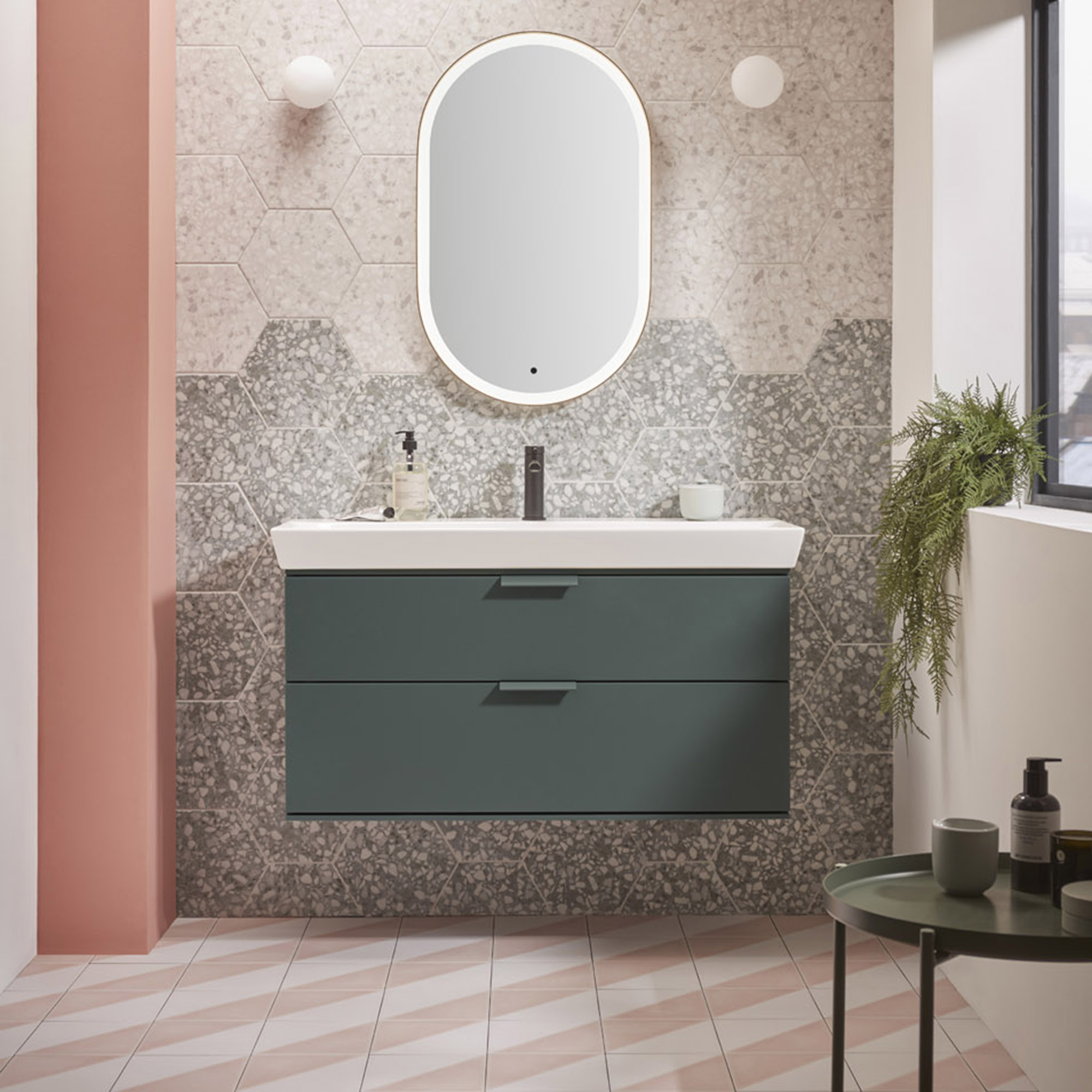 Baño moderno con mueble flotante de color verde, azulejos hexagonales en la pared y baldosas de rayas diagonales rosas y blancas en el suelo