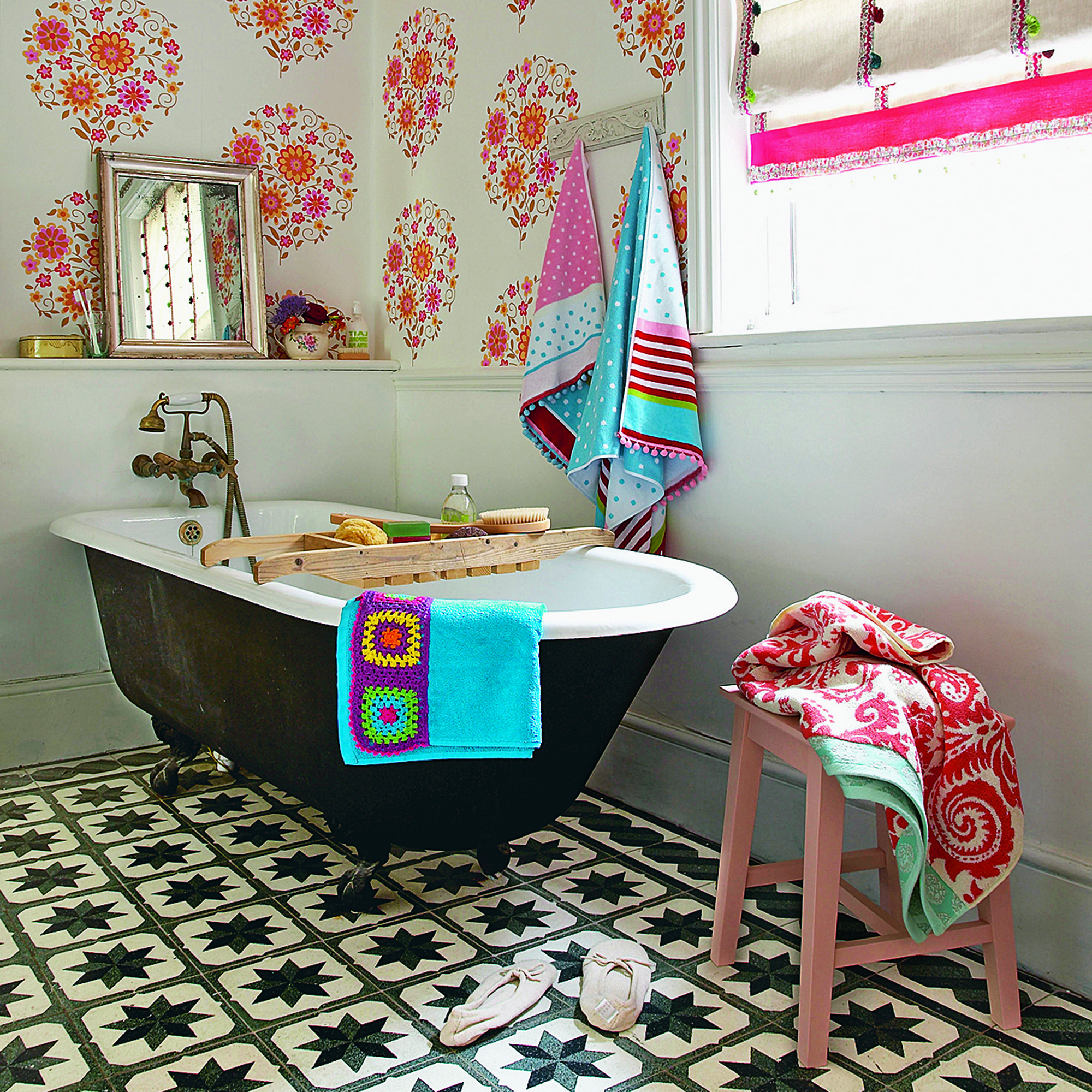 Cuarto de baño moderno y ecléctico con bañera negra, baldosas de época y un llamativo papel pintado de color rosa.